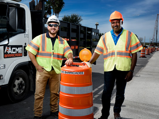 Acme Barricades standing next to an orange barrel and traffic barricade rental